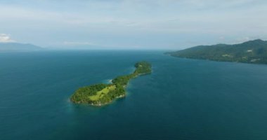 Mavi deniz ve dalgalarla çevrili yeşil ağaçları olan tropik bir ada. Mavi gökyüzü ve bulutlar. Samal Adası. Davao, Filipinler.