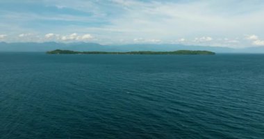 Okyanus dalgaları ve tropikal ada. Mavi gökyüzü ve bulutlar. Samal, Davao. Filipinler.