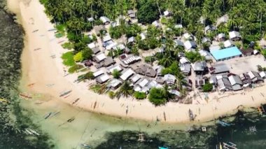 Turkuaz su ve beyaz sahilde balıkçı tekneleri. Tropik adanın üzerindeki evler ve ağaçlar. Mindanao, Filipinler. Büyütme görünümü.