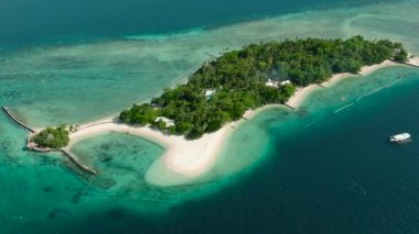 Kumlu kıyı şeridi olan adanın üst manzarası, mavi denizin üzerinde yüzen tekne. Samal, Davao. Filipinler. Deniz Burnu.