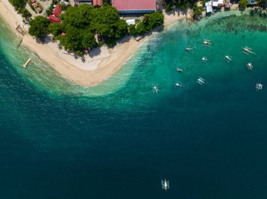 Turkuaz su ve teknelerin üzerine güneş ışığı yansıtan beyaz kumlu plaj. Samal Adası. Davao, Filipinler.