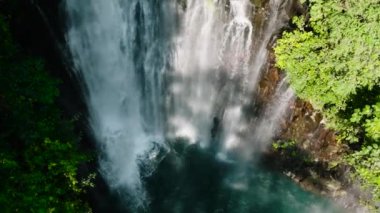 Ağaçlı Tinago Şelalesi ve güneş ışığı yansımalı doğal yapraklar. Lanao del Norte, Filipinler. Yavaş çekim.