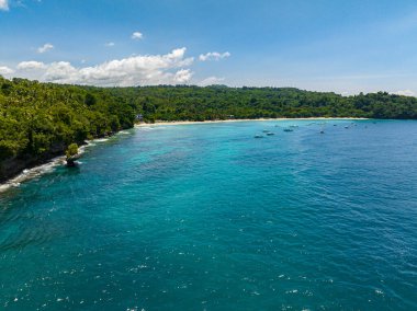 Beyaz kumlu ve okyanus dalgalı bir sahil. Gök mavisi suyun üzerinde yüzen tekneler. Samal, Davao. Filipinler.