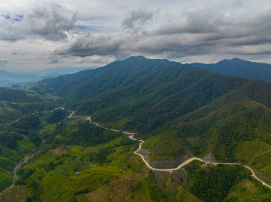 Tropik dağ yolu ve yeşil tepeler. Dağ yağmur ormanları ve mavi gökyüzü ve bulutların altındaki vadi. Mindanao, Filipinler.