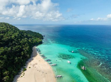 Beyaz kumda okyanus dalgaları, berrak turkuaz suyun üzerinde yüzen tekneler. Puka Deniz Kabuğu Sahili. Boracay, Filipinler.