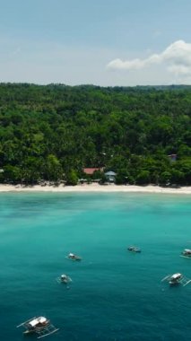Beyaz kumlu ve okyanus dalgalı bir sahil. Gök mavisi suyun üzerinde yüzen tekneler. Samal, Davao. Filipinler. Dikey görünüm.