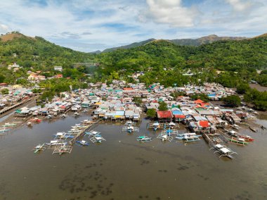 Balıkçı tekneleri ve dikiş evleri. Dağ yamacında yeşil bitkilerle dolu bir kasaba. Koron. Palawan, Filipinler.