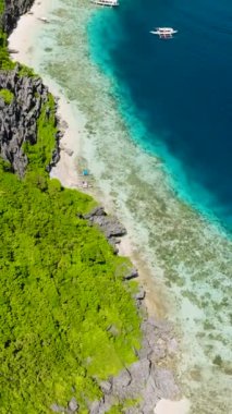 Tekneler beyaz kumsala gidiyor. Tapiutan adasıyla çevrili mavi deniz. El Nido, Palawan. Filipinler. Dikey görünüm.