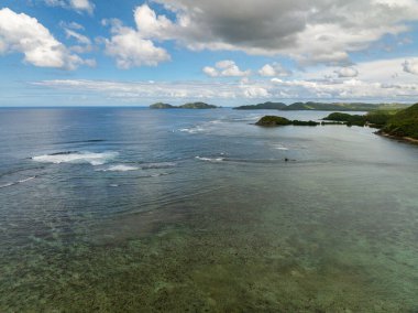 Mavi gökyüzü ve bulutların altında okyanus dalgaları ve mercanlar. Busuanga, Palawan. Filipinler.
