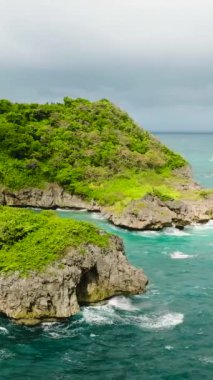 Güzel deniz dalgaları bulutlu gökyüzünün altında kayalara ve adacıklara çarpıyor. Boracay, Filipinler. Dikey görünüm.