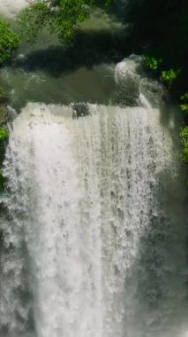 Hikong Alo Şelalesi 'nin yavaş çekimde güneş ışığı altında çağlayan sular. Sebu Gölü. Mindanao, Filipinler. Dikey görünüm.