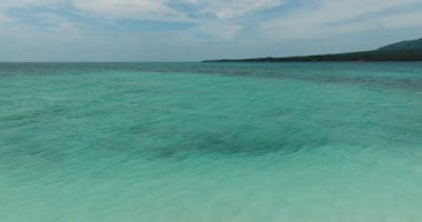 Yeşil renkli kristal berrak deniz suyu. Mavi gökyüzü ve bulutların altında dalgalar. Camiguin, Filipinler.