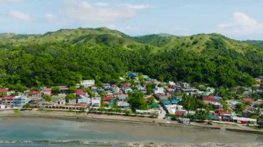 Yeşil dağların tropikal manzarası ve kıyıdaki küçük kasaba. Santa Fe, Tablas, Romblon. Filipinler.