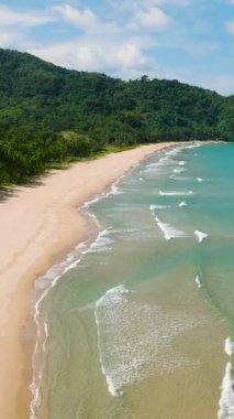 Kumlu sahil üzerindeki okyanus dalgalarının havadan görünüşü. Duli Sahili. Mavi gökyüzü ve bulutlar. El Nido, Palawan. Filipinler. Dikey görünüm.