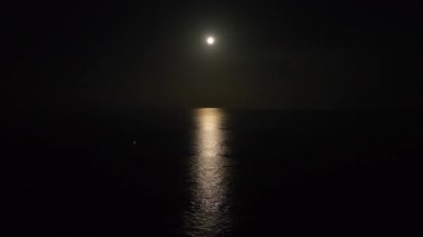 Tüyler ürpertici bir gece sahnesinde, açık, büyük bir ay okyanusun üzerinde parlıyor. Gece sahnesi.