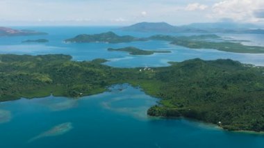 Kartallar yağmur ormanları olan tropikal adalara bakar. Mavi deniz yüzeyi, mavi gökyüzü ve bulutlar. Deniz Burnu. Mindanao, Filipinler.