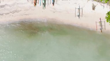 Beyaz kumlu sahildeki teknelerin üst manzarası. Suyun ve dalgaların üzerinde güneş yansıması. Carabao Adası, Romblon. Filipinler.
