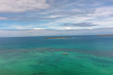 Turquoise sea water with coral reefs and tourist boat. Tropical island under the blue sky and clouds. Bantayan, Cebu. Philippines. clipart