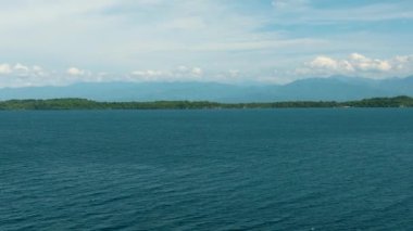 Okyanus dalgaları ve tropikal ada. Mavi gökyüzü ve bulutlar. Samal, Davao. Filipinler.