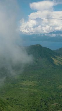 Yeşil ağaçları, ormanı ve ormanı olan tropik bir dağ. Mavi gökyüzü ve bulutlar. Camiguin Adası. Filipinler. Dikey video.
