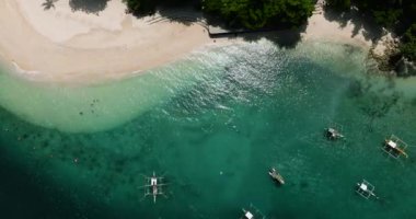 Turkuaz deniz suyu ve beyaz sahilde dalgalar. Güneş ışığı teknelere yansıyor. Samal Adası. Davao, Filipinler.