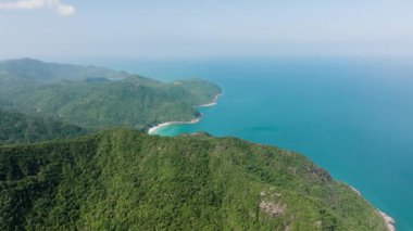 Bereketli yeşil tepeler parlak bir gökyüzünün altında berrak okyanus sularıyla buluşuyor. Ko Pha Ngan, Tayland.