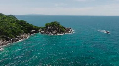 Yoğun yeşil bitki örtüsü olan küçük bir ada güneşli bir gökyüzünün altında turkuaz sularla çevrili. Koh Tao, Tayland.