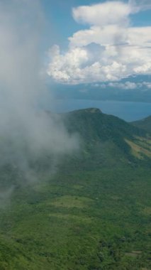 Yeşil ağaçları, ormanı ve ormanı olan tropik bir dağ. Mavi gökyüzü ve bulutlar. Camiguin Adası. Filipinler. Dikey video.