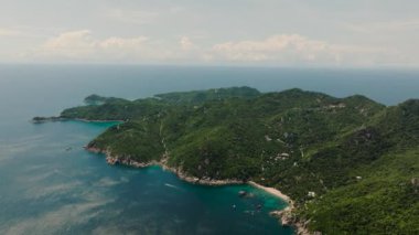 Parlak güneşli bir gökyüzünün altında denizin mavi sularına yuvarlanan yeşil tepeli geniş bir sahil şeridi. Koh Tao, Tayland.