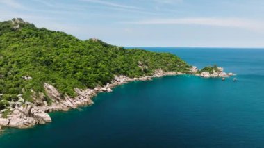 Parlak yeşil tepeleri olan Rocky sahili güneşli bir gökyüzünün altında derin mavi denizle buluşuyor. Koh Tao, Tayland.