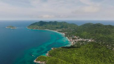 Yeşil tepelerin, canlı turkuaz suların ve etrafa saçılmış küçük teknelerin bulunduğu bir kıyı manzarası. Koh Tao, Tayland.