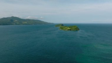 Derin mavi denizle çevrili tropikal bir ada. Mavi gökyüzü ve bulutlar. Samal Adası. Davao, Filipinler. Deniz Burnu.