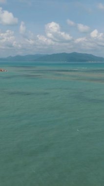 Turkuaz deniz, yeşil kıyı şeridi ve bulutlu bir gökyüzünün altında uzak dağlar. Ko Samui, Tayland.