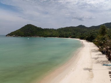 Turkuaz suyu ve sakin bir gökyüzü olan yemyeşil tepelerle çevrili kıvrımlı beyaz bir kumsal. Ko Pha Ngan, Tayland.