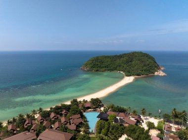 Turkuaz sularla çevrili yemyeşil bir adaya ve parlak güneşli bir gökyüzünün altındaki tatil köylerine uzanan bir kumluk. Ko Pha Ngan, Tayland.