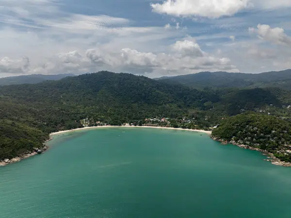 Zümrüt yeşili suları olan yemyeşil bir körfez. Parçalı bulutlu bir gökyüzünün altında tepelerle çevrili. Ko Pha Ngan, Tayland.