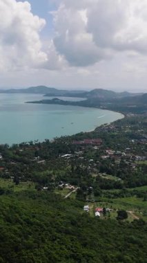 Yeşil tepeleri yuvarlanan kıyı manzarası, turkuaz deniz ve parlak bir gökyüzünün altında dağınık evler. Maenam, Ko Samui, Tayland.