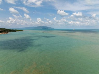 Turkuaz deniz suları, gölgeli bölgeleri, uzak dağları ve tüylü bulutlarla dolu berrak mavi gökyüzü. Koh Samui, Tayland.