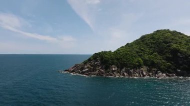 Mavi okyanusla buluşan canlı yeşil tepeler ve parlak güneşli gökyüzünün altında açık bir ufuk. Koh Tao, Tayland.