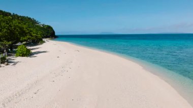 Parlak bir gökyüzünün altında yemyeşil ve kristal berrak turkuaz sularla çevrili el değmemiş beyaz kumlu sahil. Cobrador Adası, Romblon, Filipinler.