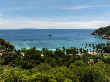 Bereketli yeşillik, turkuaz su ve uzaktaki dağınık teknelerle çevrili tropikal kıyı şeridi. Koh Tao, Tayland.