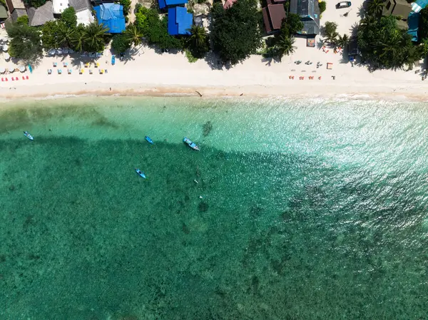 Renkli şemsiyeler, turkuaz su ve küçük demirli teknelerle dolu kumlu bir plaj hizasında. Koh Tao, Tayland.