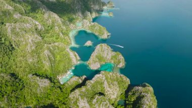 Kireçtaşı tepeleriyle çevrili turkuaz lagünlerin üzerinden geçen teknelerin üst görüntüsü. Coron, Palawan, Filipinler.