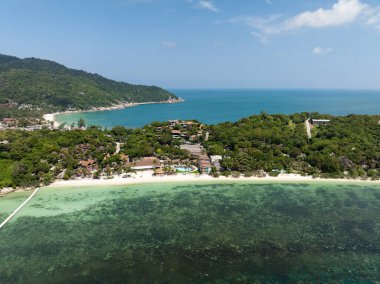 Açık bir gökyüzünün altında turkuaz deniz bulunan canlı yeşilliklerle dolu küçük bir sahil köyü. Ko Pha Ngan, Tayland.