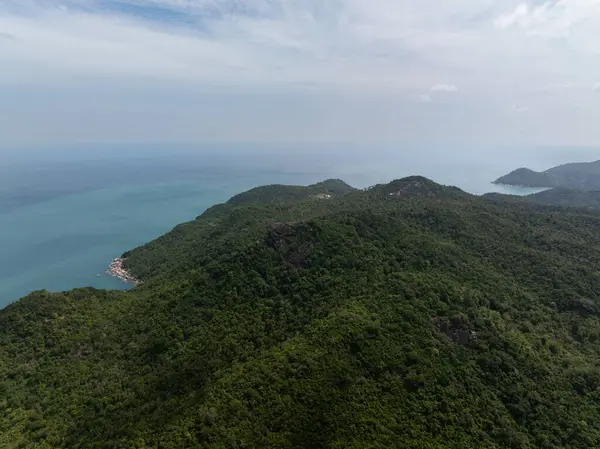 Yeşillik yeşil tepelerin panoramik görüntüsü parçalı bulutlu bir gökyüzünün altında mavi okyanus ufkuyla buluşuyor. Ko Pha Ngan, Tayland.