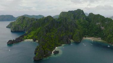Miniloc Adası 'ndaki yoğun kireçtaşı kaya ve kayalıkları. Beyaz kumsallardaki turist tekneleri. El Nido, Filipinler,