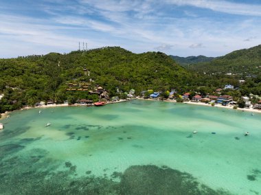 Yeşil tepeler ve parlak bir gökyüzü arasında yuva yapmış, sakin sahil güzelliğini gösteren bir köyü olan turkuaz körfez. Koh Tao, Tayland.