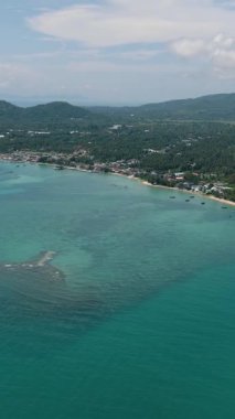 Kumlu bir sahil manzarası, turkuaz sular ve kıyı şeridi boyunca yemyeşil bir su. Ko Samui, Tayland.