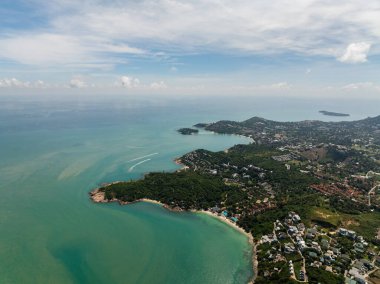Panoramik kıyı manzarası turkuaz sular, yemyeşil alanlar ve kıyı boyunca dağınık binalar sergiliyor. Bo Put. Koh Samui, Tayland.