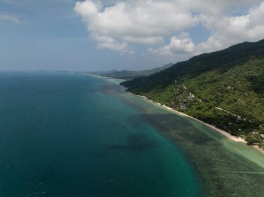 Yoğun yeşil ormanı, dolambaçlı yolu ve ufka uzanan berrak turkuaz suları olan uzak bir sahil şeridi. Ko Pha Ngan, Tayland.
